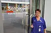 Helsearbeider i blå uniform ved glassdør til en sengepost.