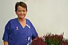 Smilende helsearbeider i blå uniform ved blomstrende planter.