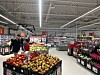 Kunder ved en stor frukt- og grønnsaksdisk i en dagligvarebutikk.