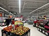 Kunder ved en stor frukt- og grønnsaksdisk i en dagligvarebutikk.